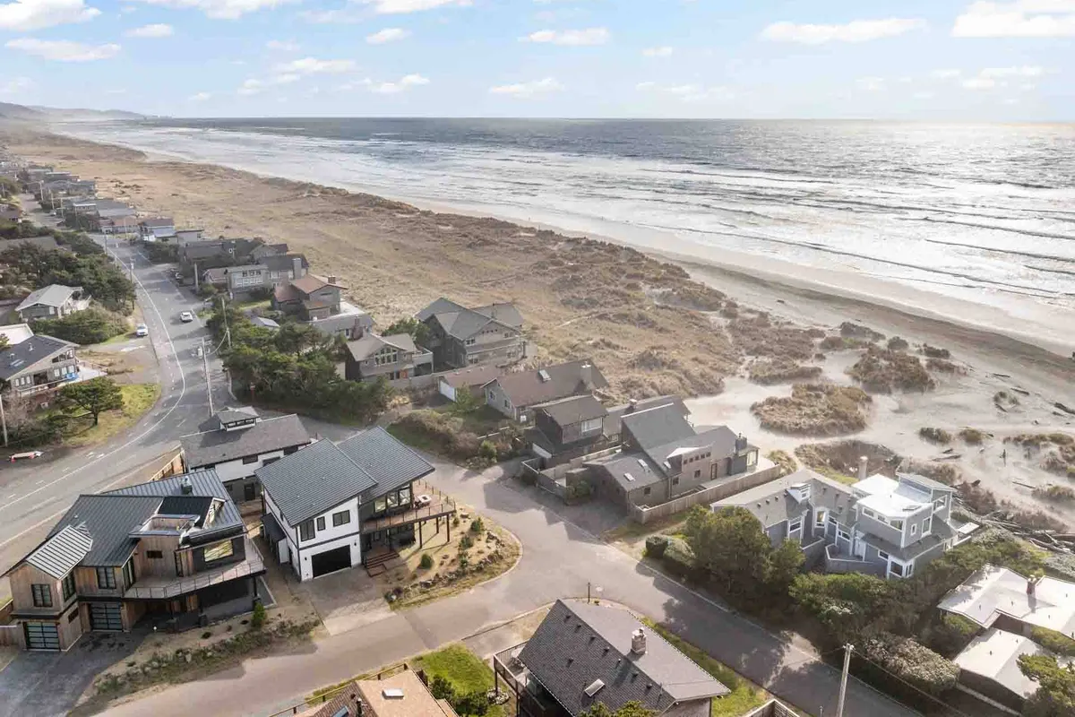 An elevated view captures the ocean, beachfront homes, and the scenic coastal road below. The mood is serene, inviting thoughts of beach walks, watching sunsets, and exploring the shore just steps away from the home.