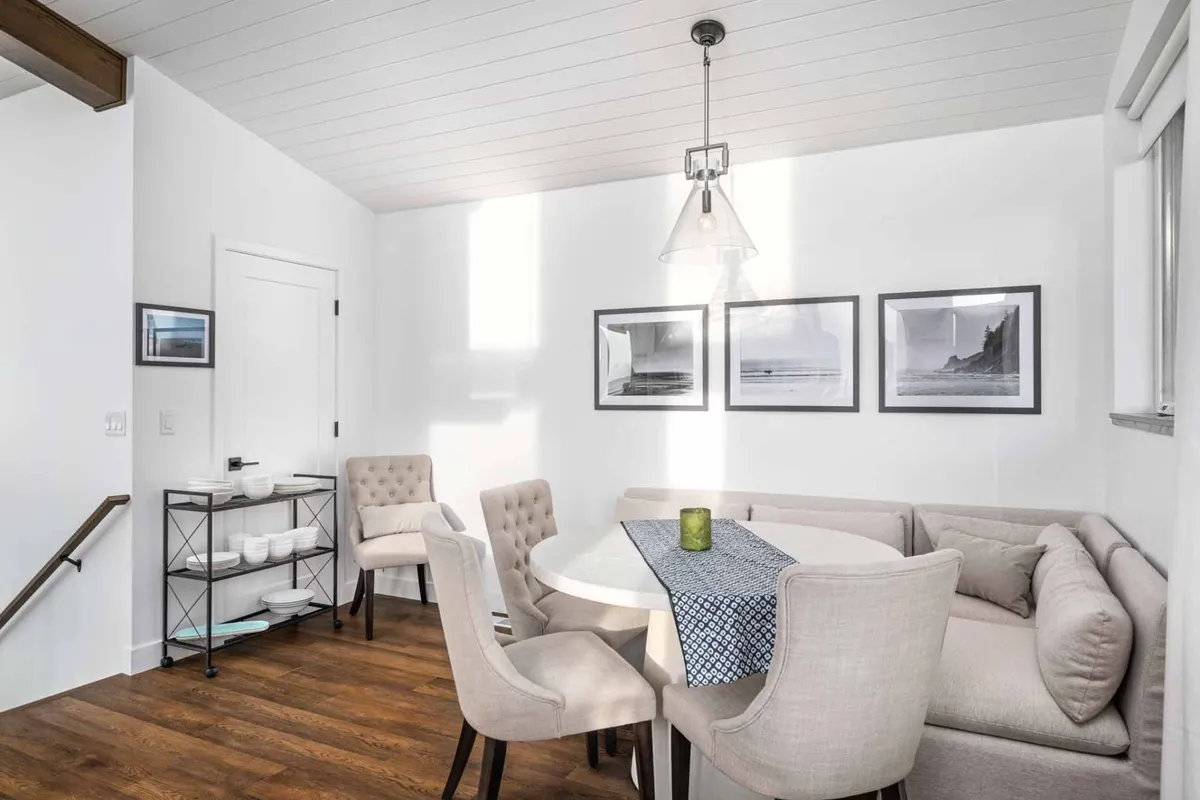 This image focuses on a cozy dining area with a round table and a comfortable corner sofa, accented by framed photographs and a modern pendant light. The space is designed for casual dining, socializing, and quiet moments, embodying a welcoming, family-friendly mood.