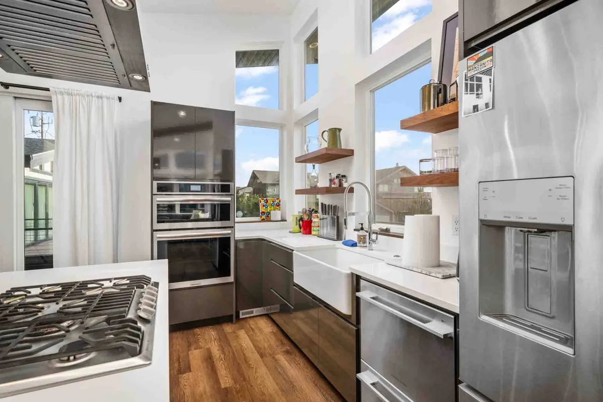 This image presents the gourmet kitchen, centered around a kitchen island with a gas stove and surrounded by sleek cabinetry and open shelving. Large windows bathe the space in sunlight, making it ideal for both culinary adventures and socializing. The layout flows naturally into adjoining living spaces.