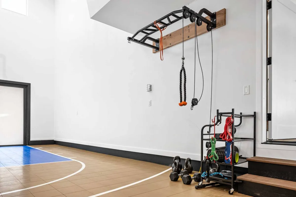 A dynamic view inside the sport court area, focusing on exercise equipment like a pull-up bar as well as the basketball court lines on the floor. The scene evokes energy and motivation, with individuals engaged in both strength training and basketball activities.